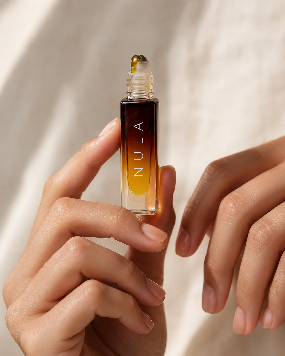 A hand holding the NULA oil roller with a golden drop on the applicator